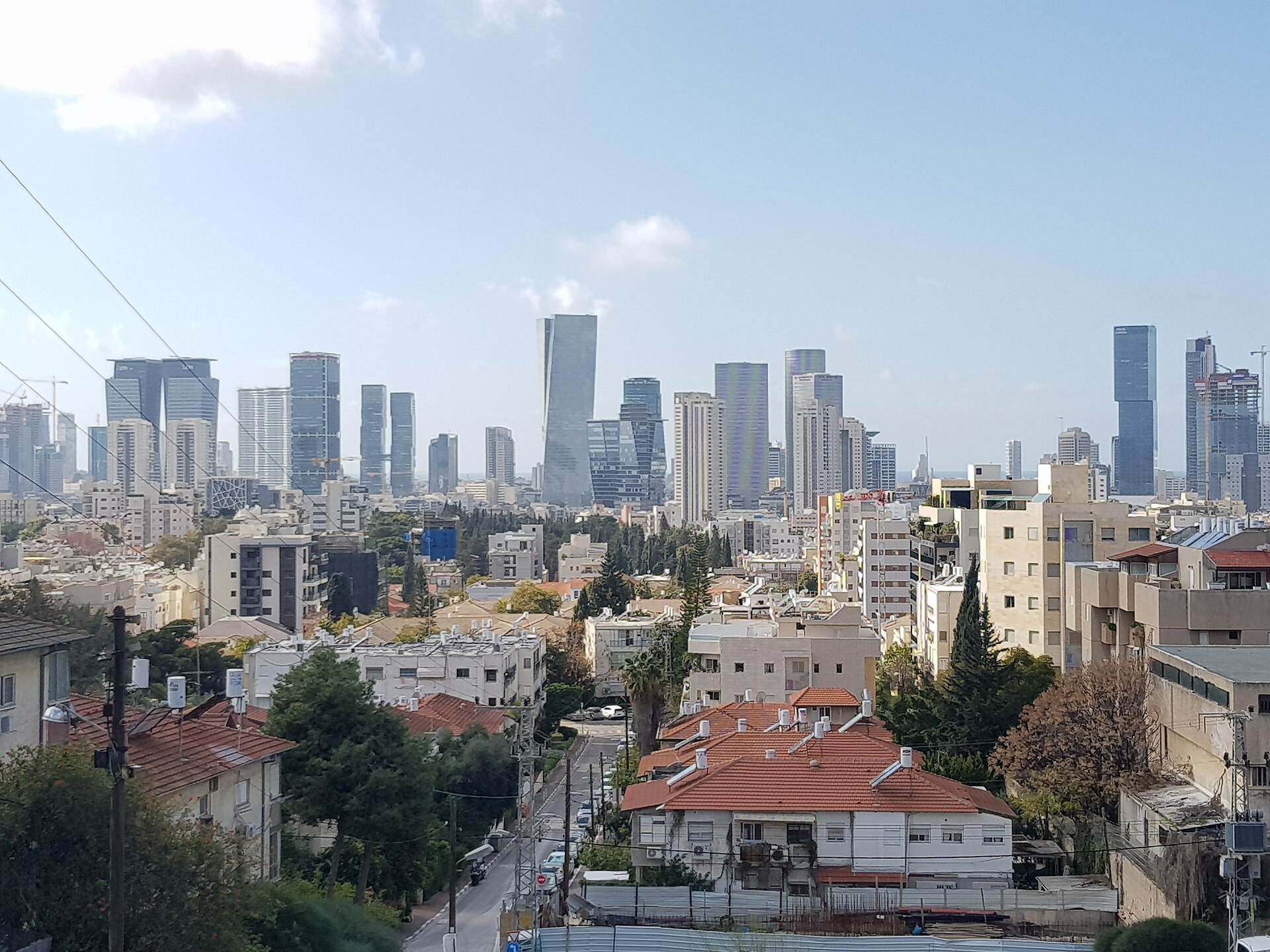 מבט מגבעת קוזלובסקי בגבעתיים: גגות רעפים, עצים, ומגדלי תל אביב באופק
